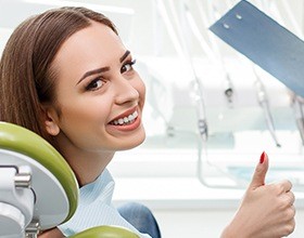 Woman in dental chair with porcelain veneers giving thumbs up