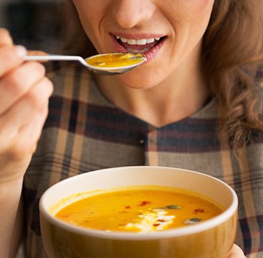 A smiling woman eating pumpkin soup
