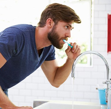 A man in pajamas brushing his teeth in front of a bathroom mirror