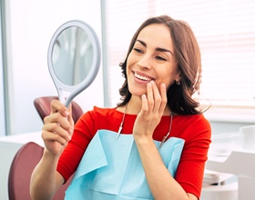 Woman admiring teeth in mirror after receiving dental bonding