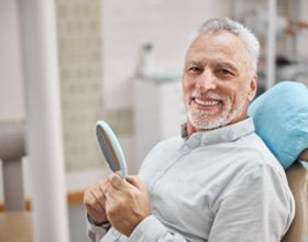 Senior man smiling while holding handheld mirror at dentist's office
