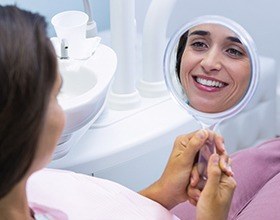 Woman looking at smile in mirror after dental bonding