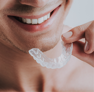 Person holding a clear mouthguard near their smile