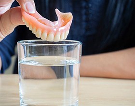 Close up of patient dropping their denture in a glass of cleaning solution