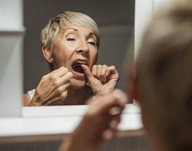 Woman flossing her all-on-4 dentures in mirror