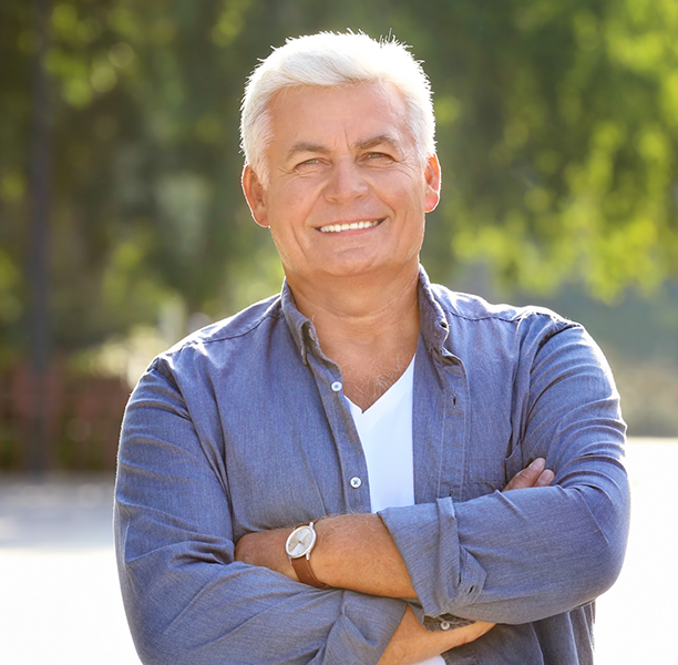 Older man smiling outdoors with his arms crossed