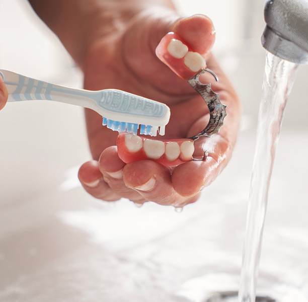 Person cleaning their denture with a toothbrush in a sink