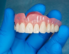 Closeup of upper arch of dentures held in blue-gloved hand