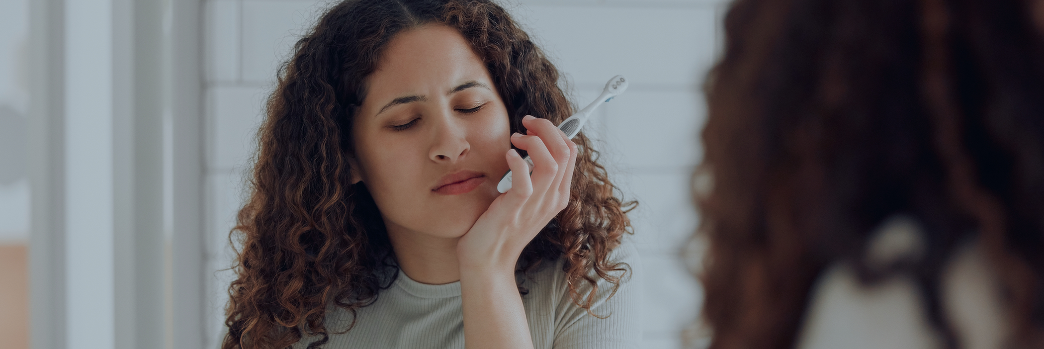Woman holding her cheek in pain before seeing an emergency dentist