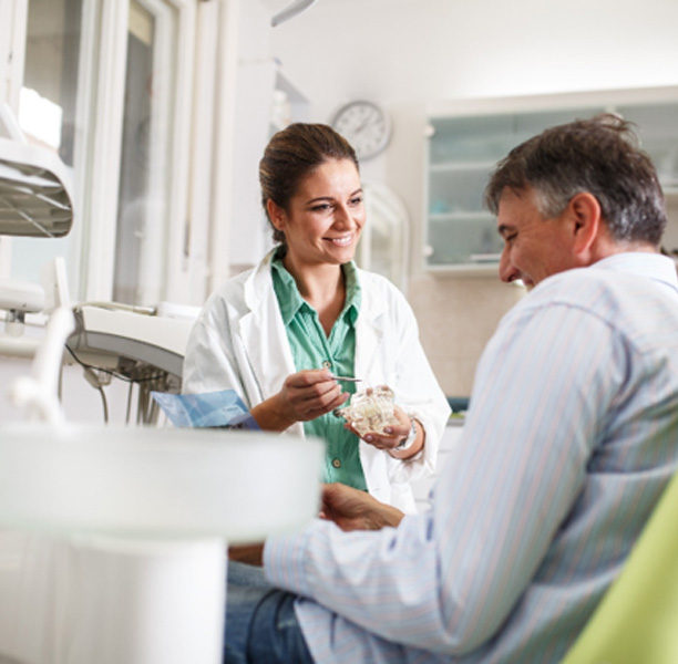 Smiling dentist showing patient model of teeth