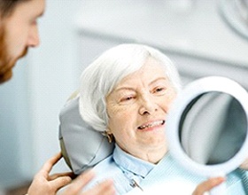 Smiling woman admiring her new dental implant supported dentures in Boca Raton