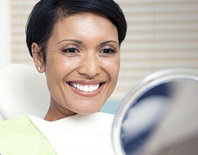 Woman looking at smile in mirror after tooth colored fillings
