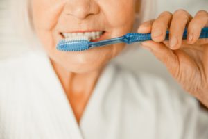 Senior woman brushing teeth to care for smile during COVID-19