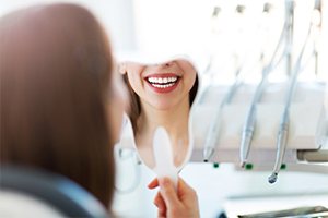 Woman with veneers in Boca Raton smiling into hand mirror 