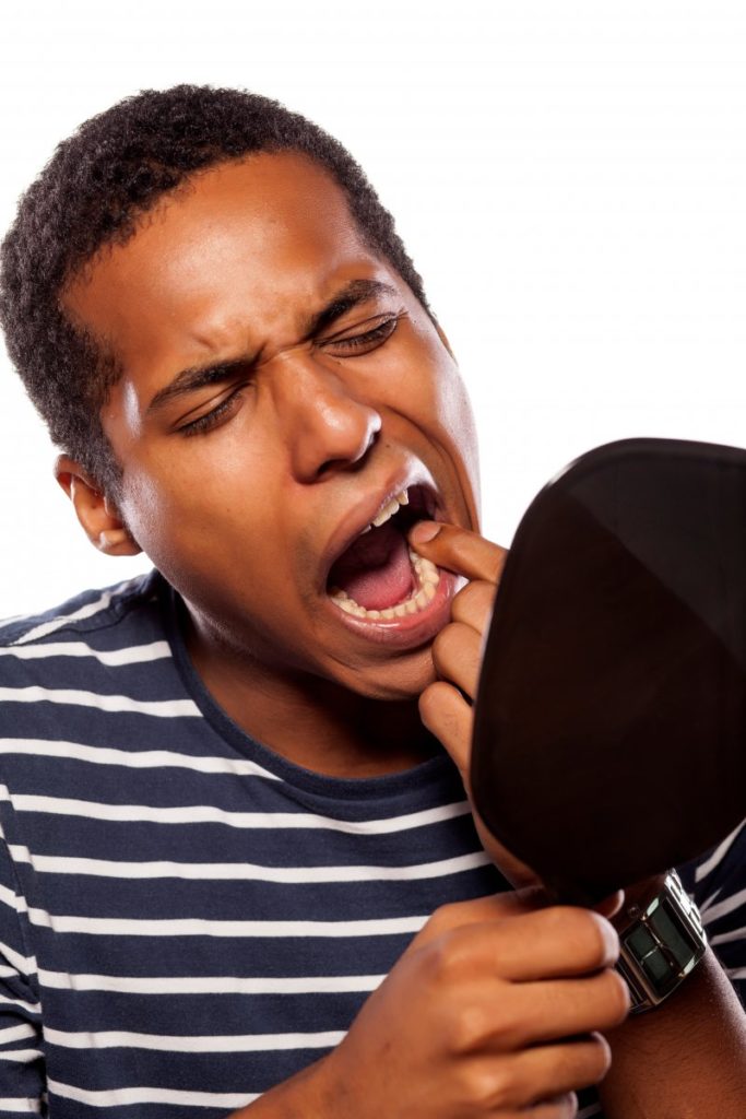 Young man checking his loose tooth in a mirror