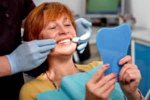 a woman smiling at her dental implants while she’s with her dentist