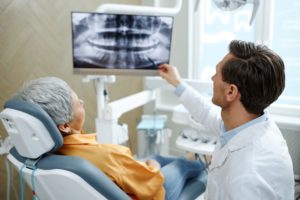 Woman in orange shirt in dentist's chair while they go look together at an x-ray of her teeth