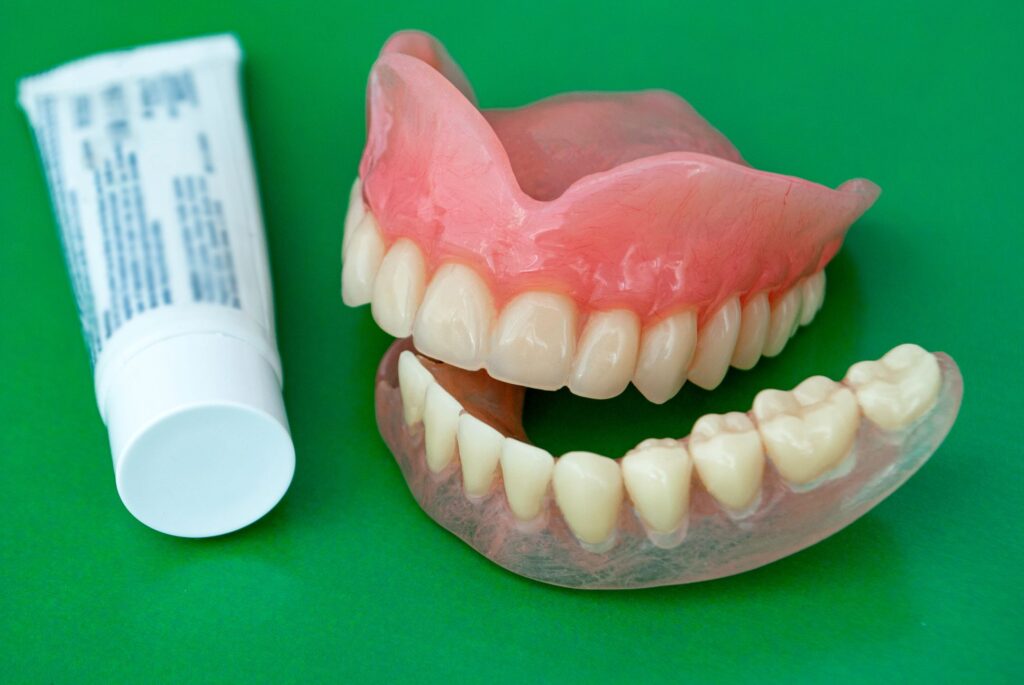 Full set of dentures next to adhesive tube on green surface